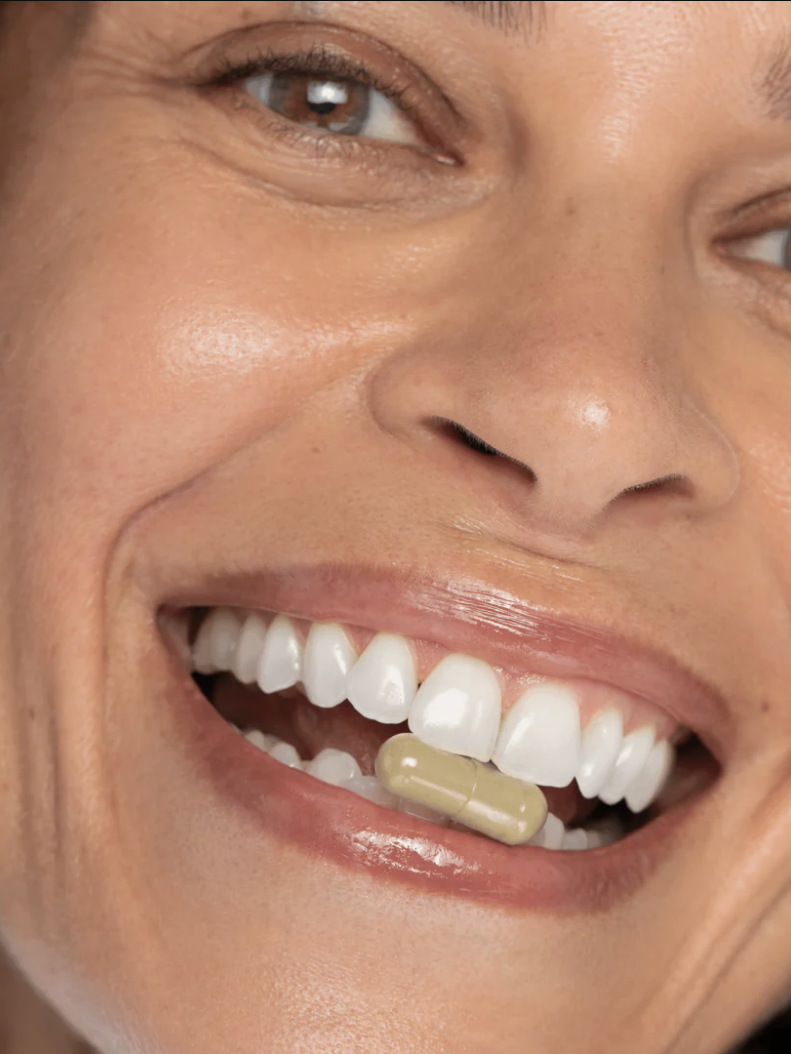 Person smiling with a pill between their teeth.
