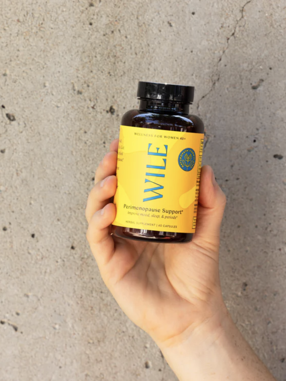 Hand holding a brown bottle labeled "Wile Perimenopause Support" against a textured gray background.