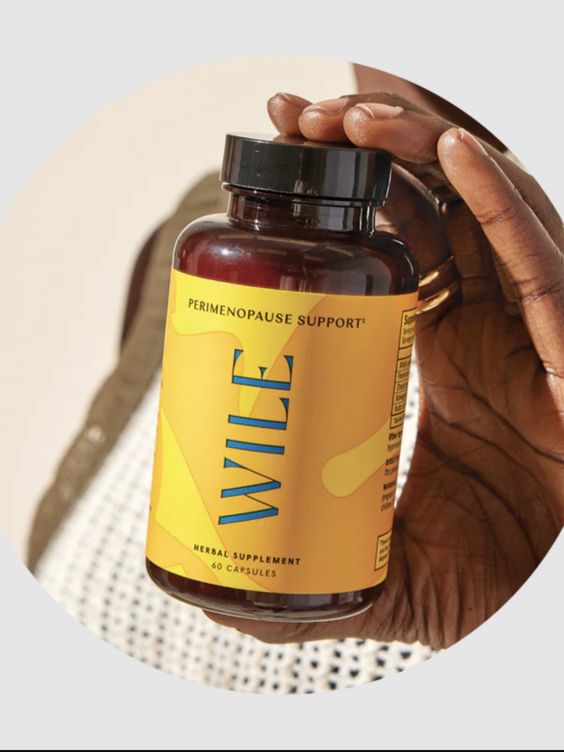 Hand holding a bottle labeled "Wile Perimenopause Support," a herbal supplement with 40 capsules, against a neutral background.