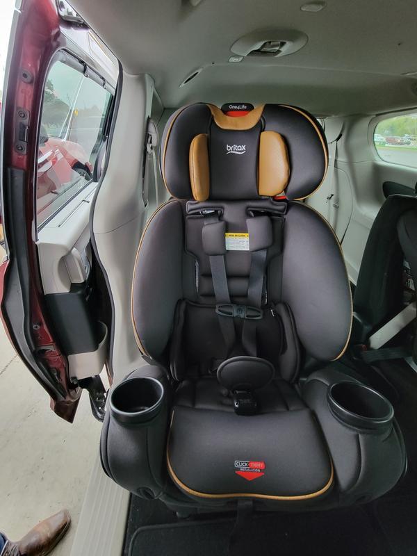 Child car seat installed in the backseat of a vehicle, showing adjustable headrest, harness, and cup holders.