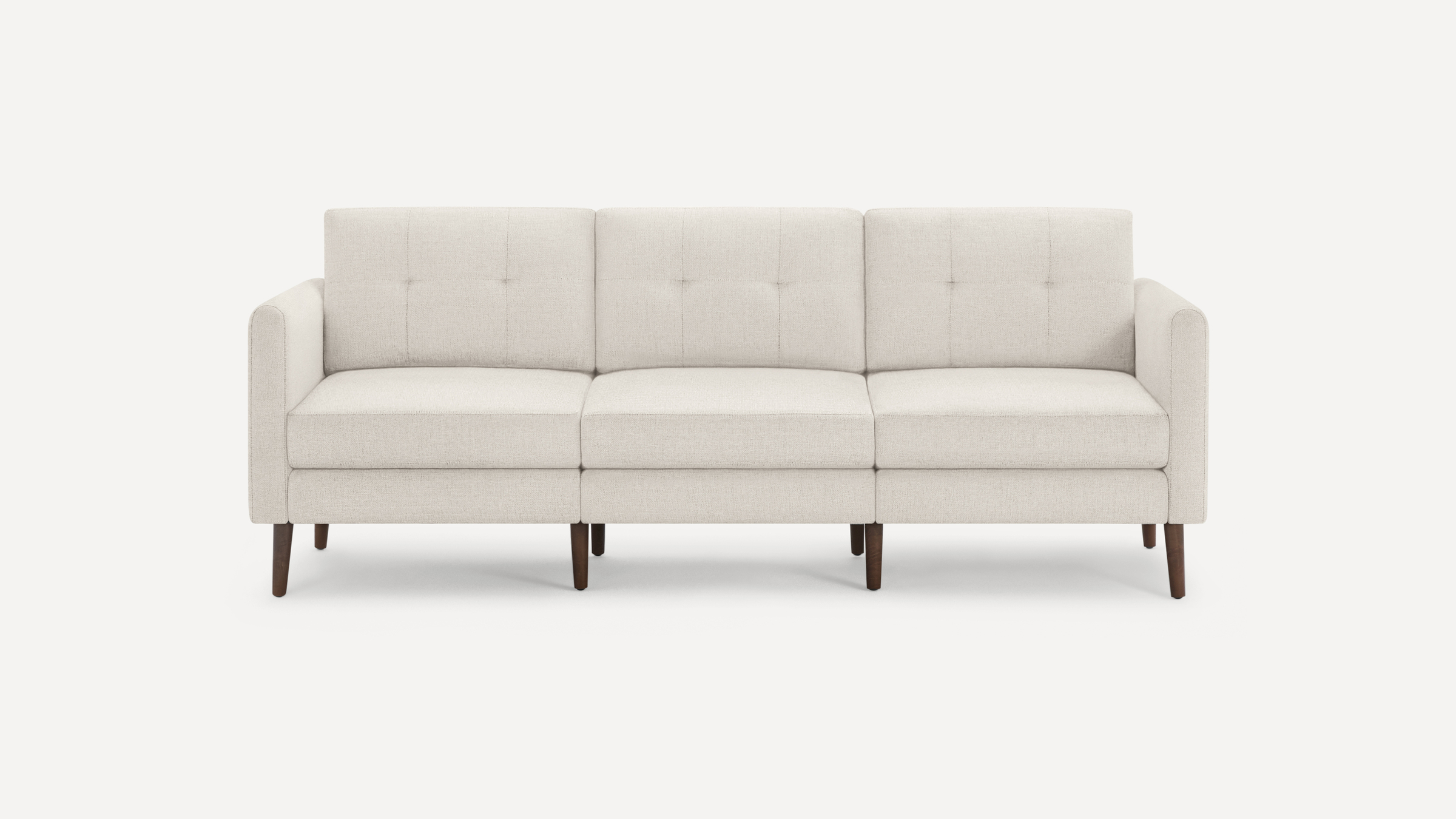 A minimalist beige sofa with three seat cushions, button tufting, and dark wooden legs is centered against a white background.