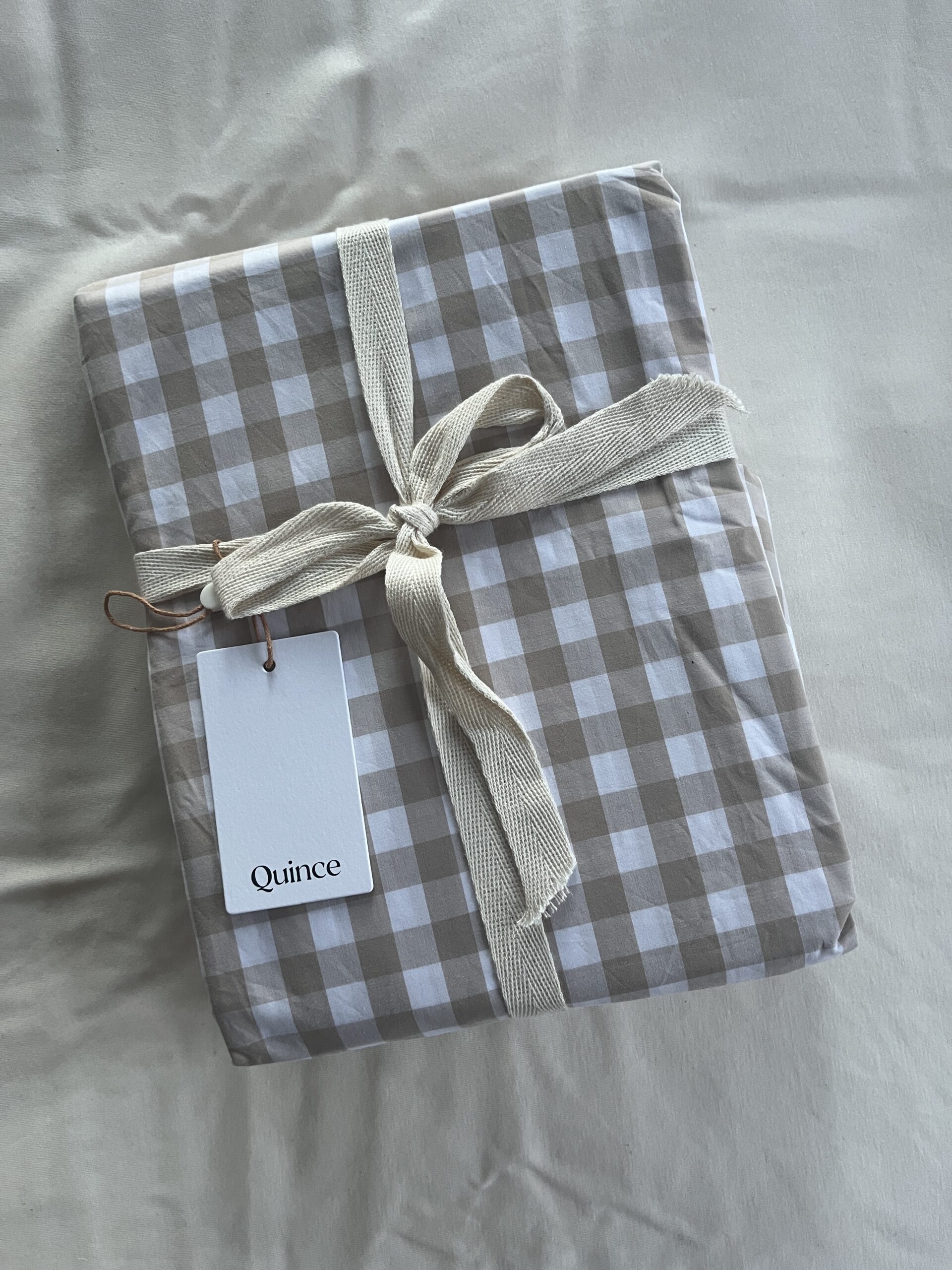 A package wrapped in checked fabric with a cream ribbon and a "Quince" tag on a plain background.