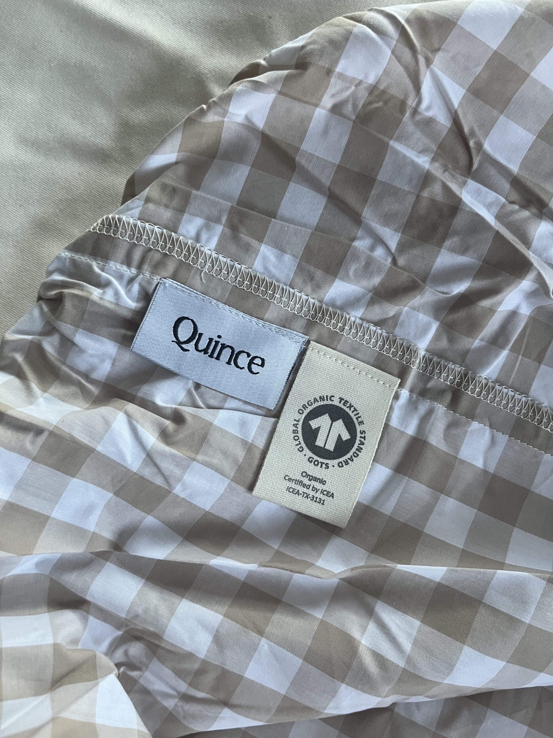 Close-up of a beige and white checkered sheet with a "Quince" brand label and a "GOTS organic textile" certification tag.