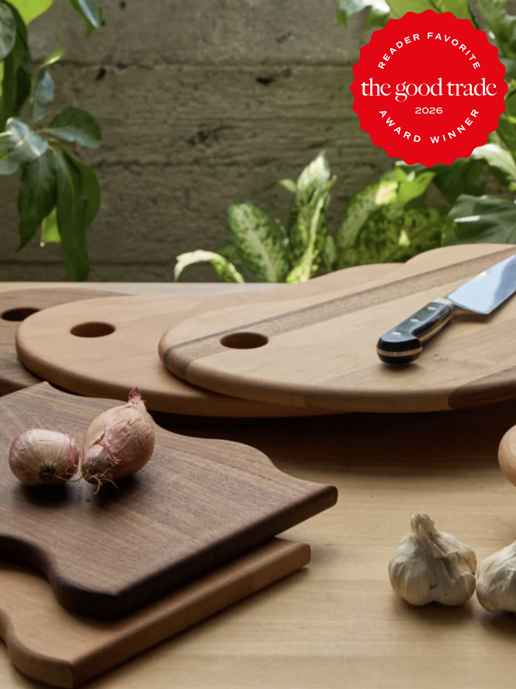 Assorted wooden cutting boards with a knife, shallots, and garlic on a kitchen counter; “The Good Trade Award Winner 2026” badge in the corner.
