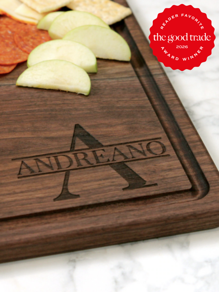 A wooden cutting board engraved with the name "Andreano," holding slices of apple, crackers, and pepperoni; a red award badge in the corner reads "The Good Trade Award Winner 2026.