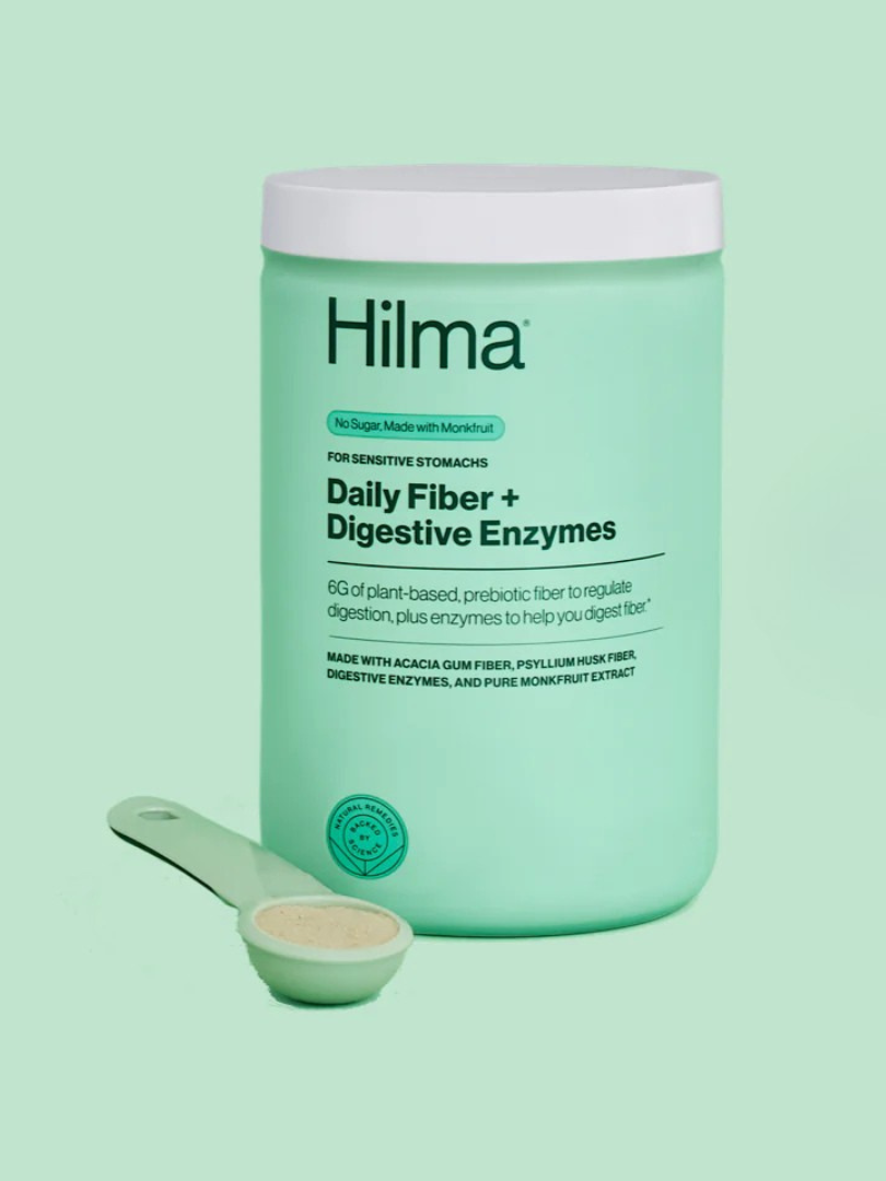 Green container of Hilma Daily Fiber + Digestive Enzymes with a serving spoon beside it, on a matching green background.