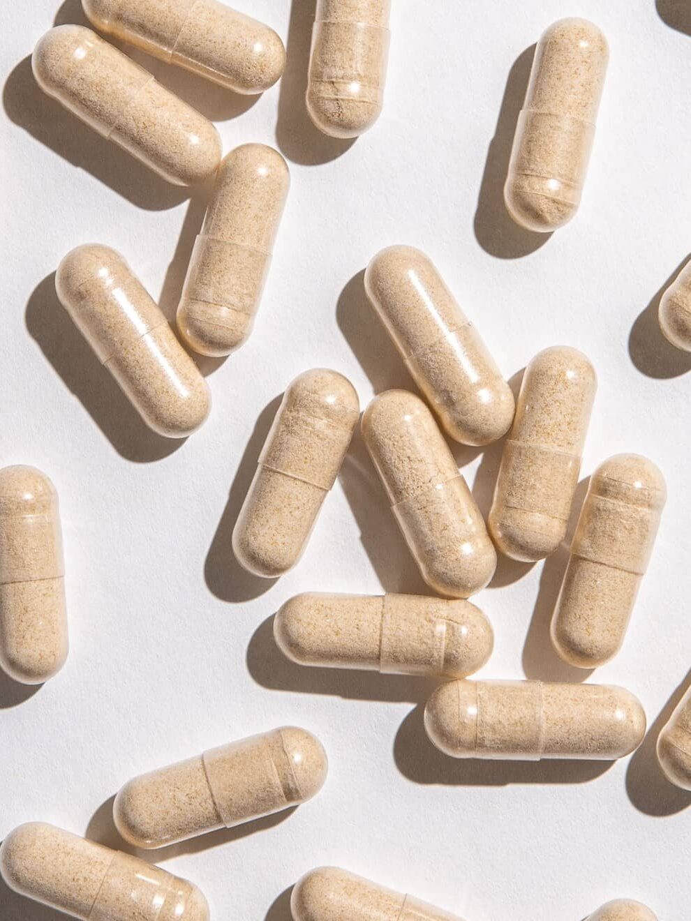 Beige capsules scattered on a white surface in bright, even lighting.