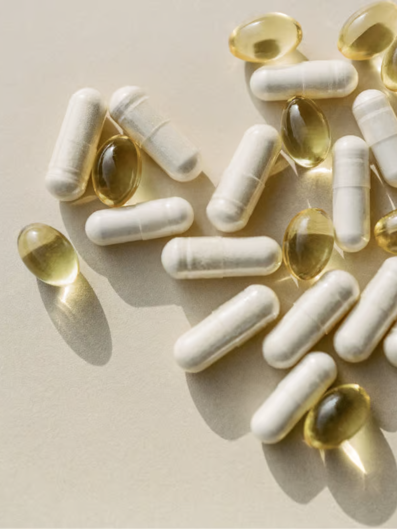 White capsules and yellow gel capsules scattered on a light surface.