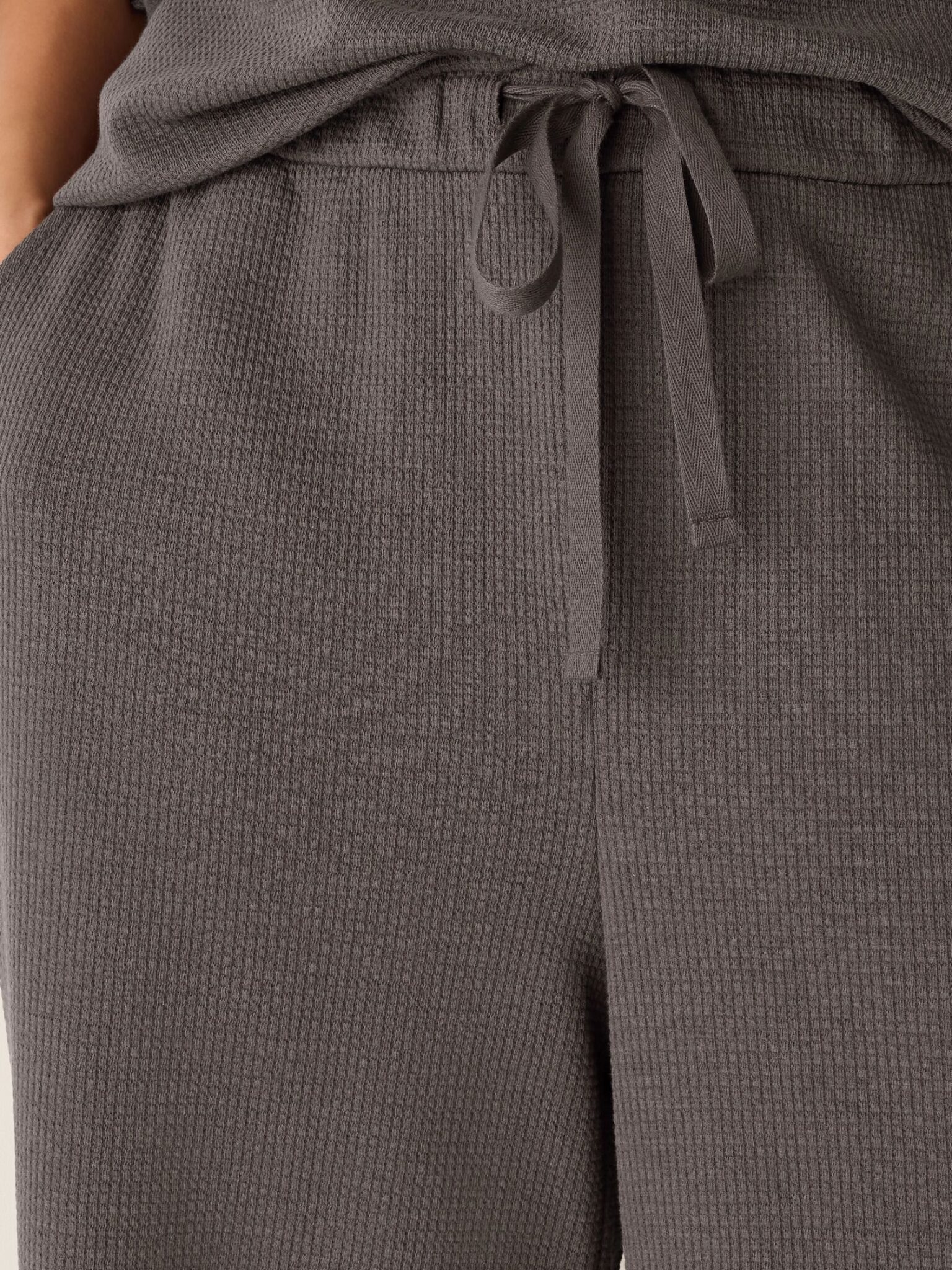 Close-up of a person wearing textured gray drawstring pants with hands in pockets.