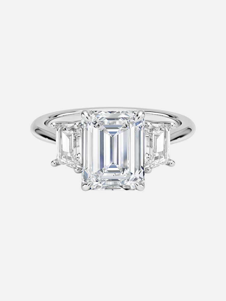 Emerald-cut diamond ring with two smaller rectangular diamonds on a silver band, displayed against a white background.