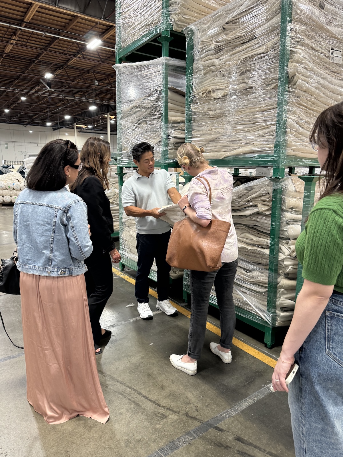 Group of people discussing a document in a warehouse, standing near large stacks of packaged goods.