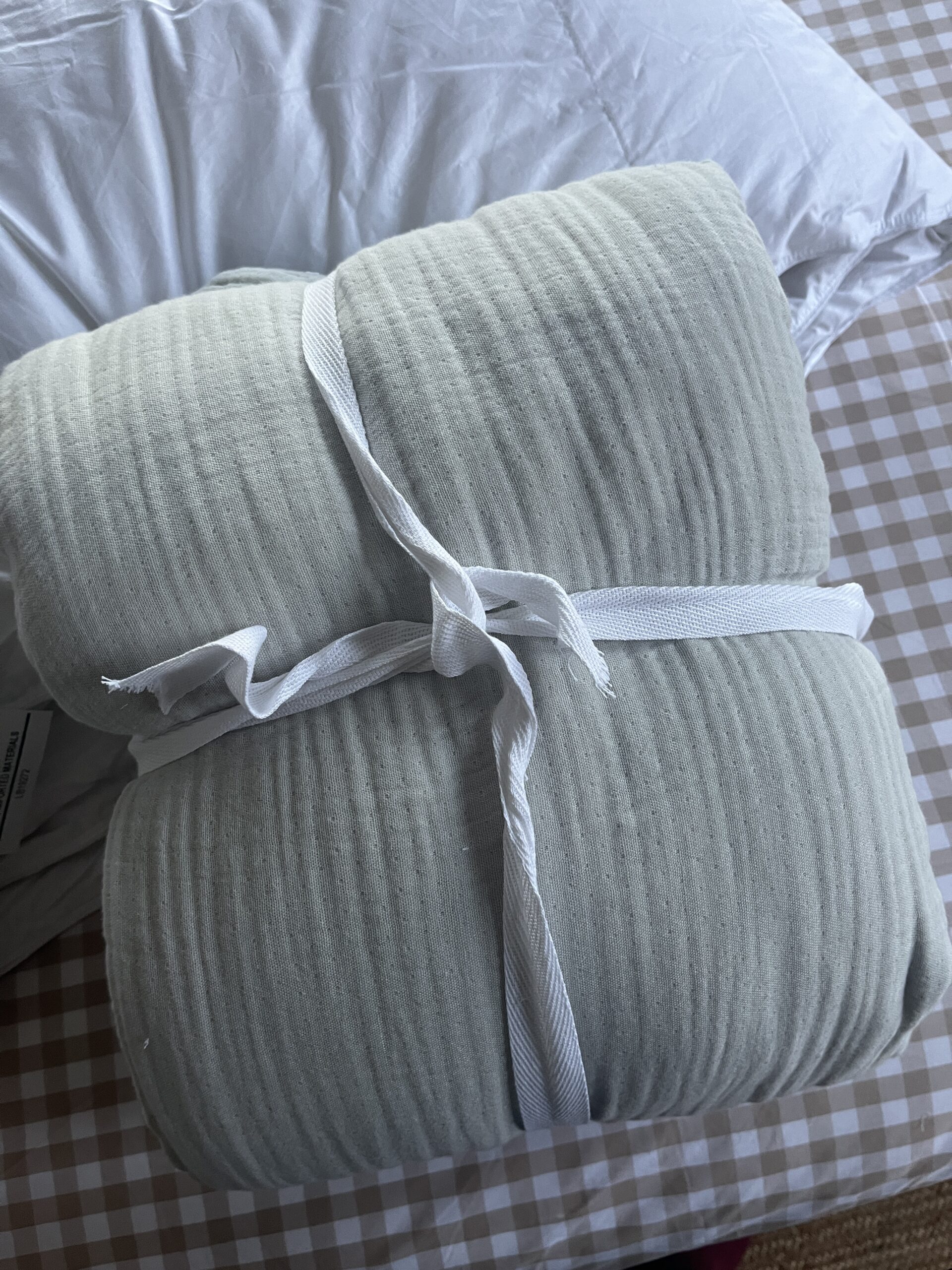 A folded, light green blanket tied with a white ribbon rests on a checked surface.