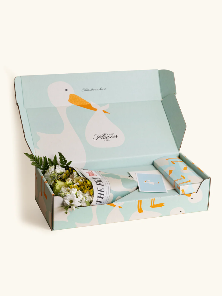 An open pastel blue gift box with a goose illustration contains a bouquet of flowers wrapped in paper, a small package, and a card.