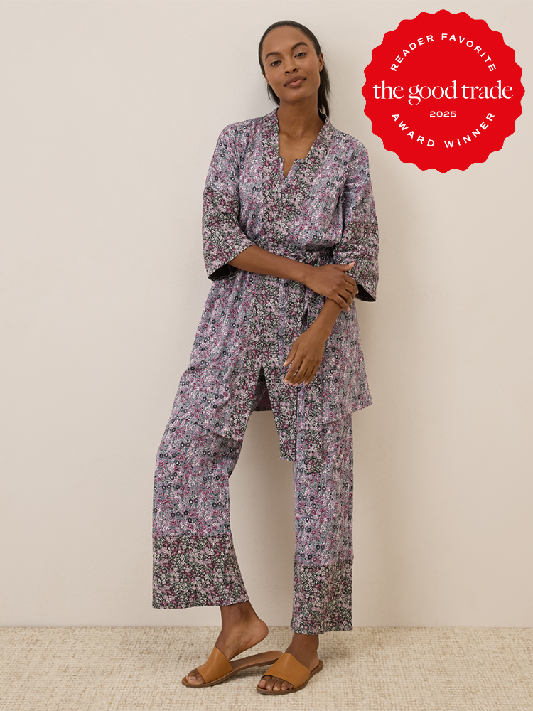 A woman stands against a plain wall wearing a floral-patterned kimono-style pajama set and tan sandals. A red "The Good Trade 2025 Award Winner" badge is displayed in the top right corner.