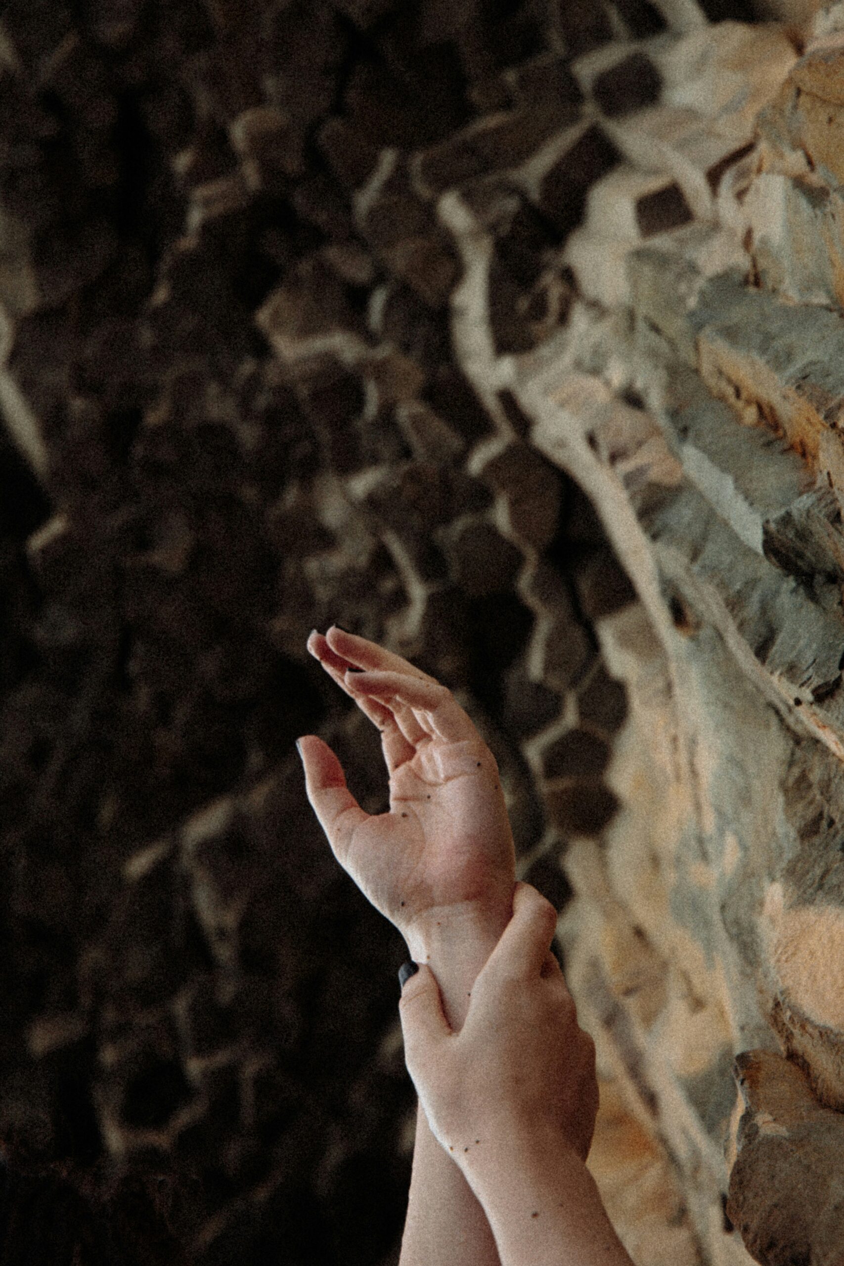 Hands reaching upward towards a textured rocky surface in a dimly lit environment.