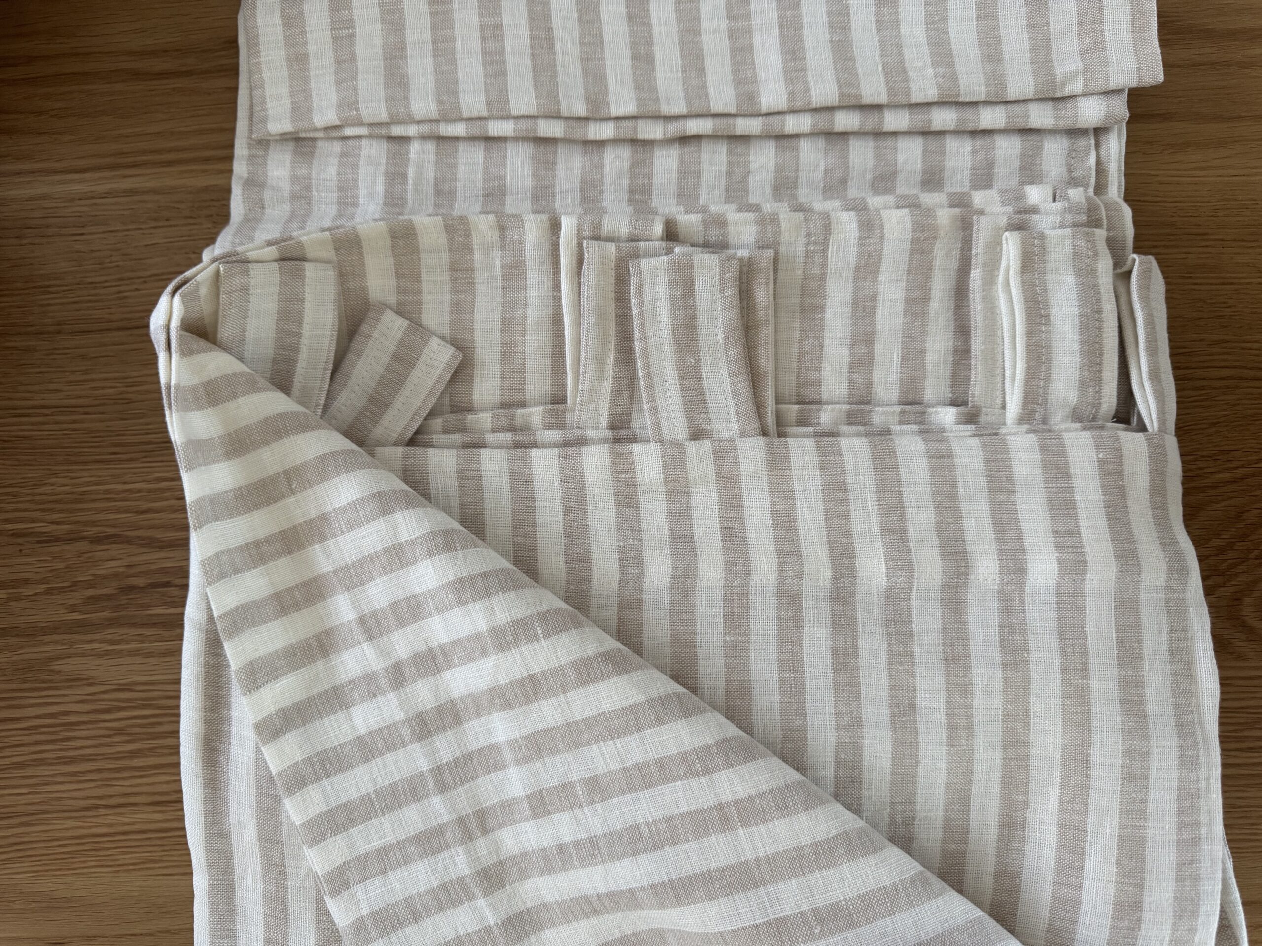 Stack of beige and white striped linen fabric folded neatly on a wooden surface.