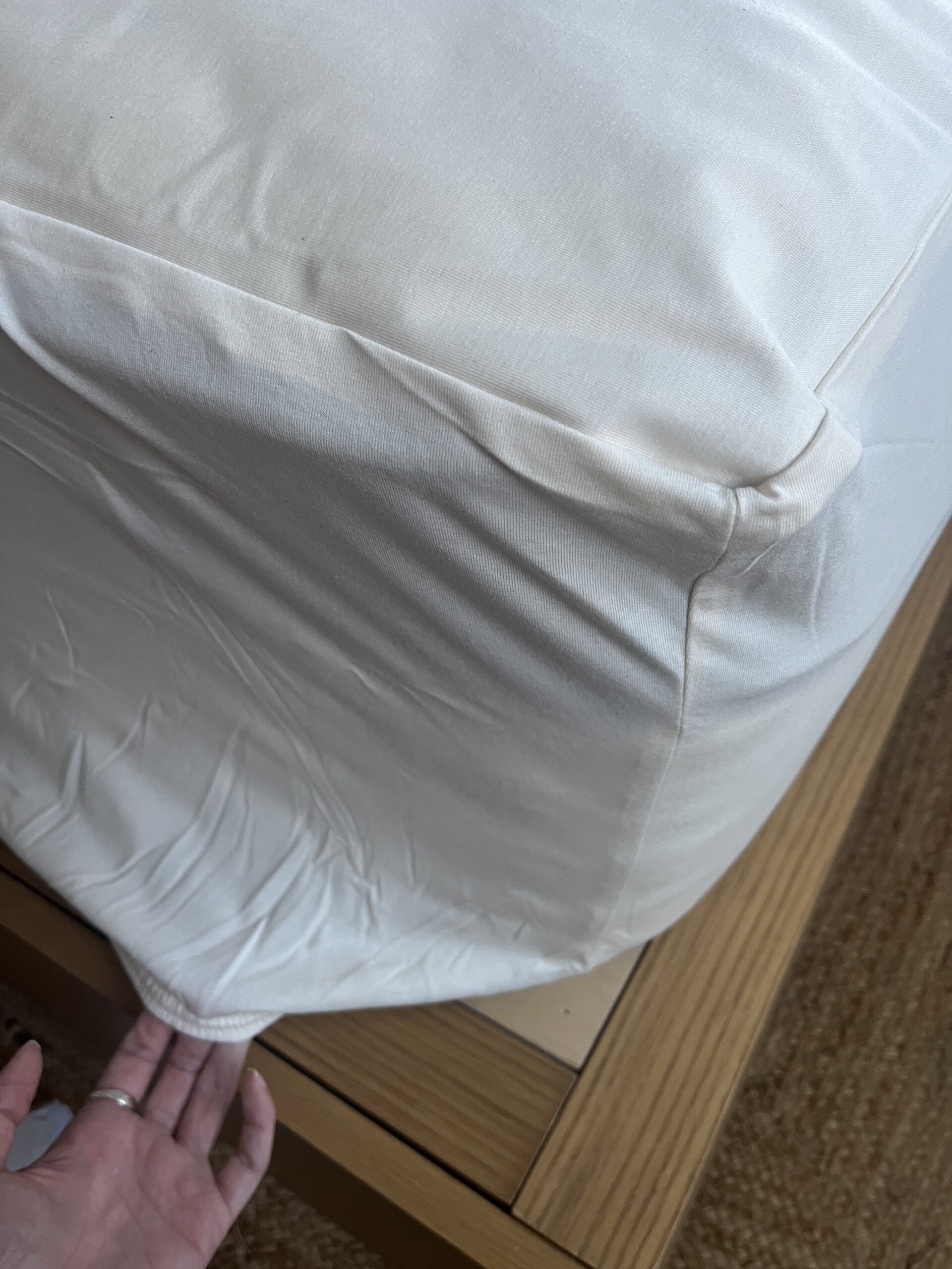 A hand adjusting a fitted white sheet on a wooden bed frame.