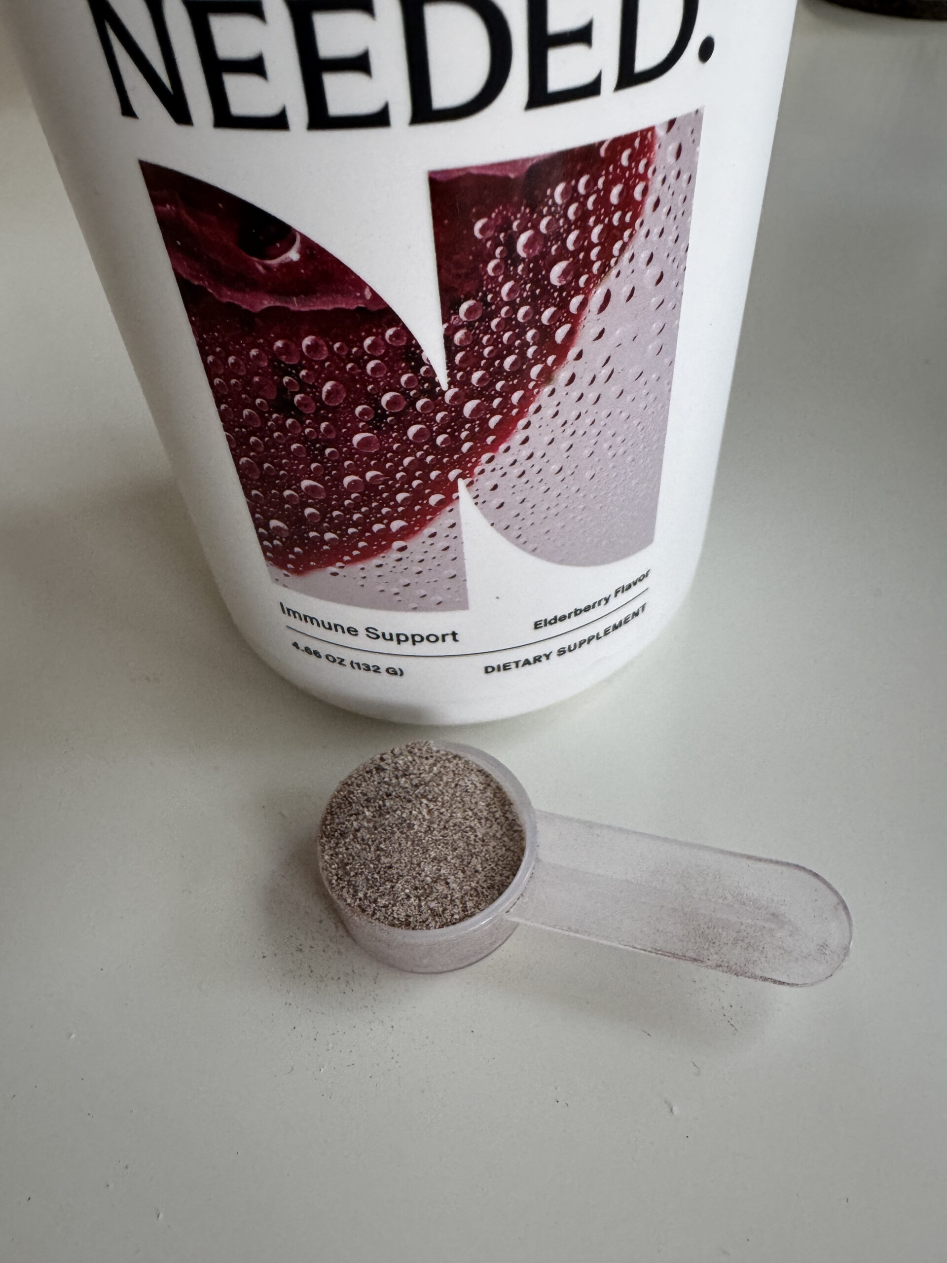 Container labeled "Immune Support" next to a scoop of powder on a white surface.