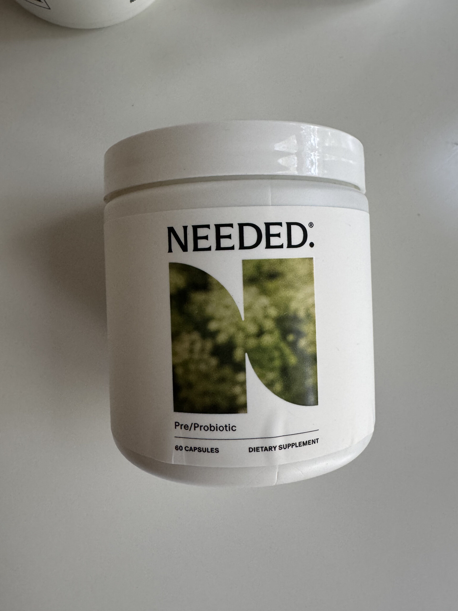 A white container labeled "NEEDED" containing pre/probiotic dietary supplement capsules.