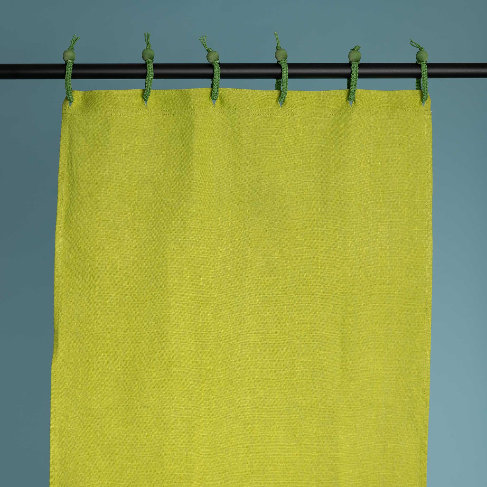 A lime green curtain with green looped ties hangs from a black rod against a teal wall.