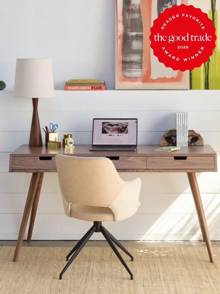 A wooden desk with a laptop, lamp, and decor items. A beige chair faces the desk. Award badge on top right corner reads "Reader Favorite, The Good Trade, 2025 Award Winner.