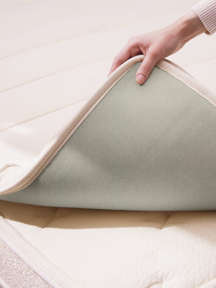 Hands adjusting a light green mattress pad on a cream-colored mattress.