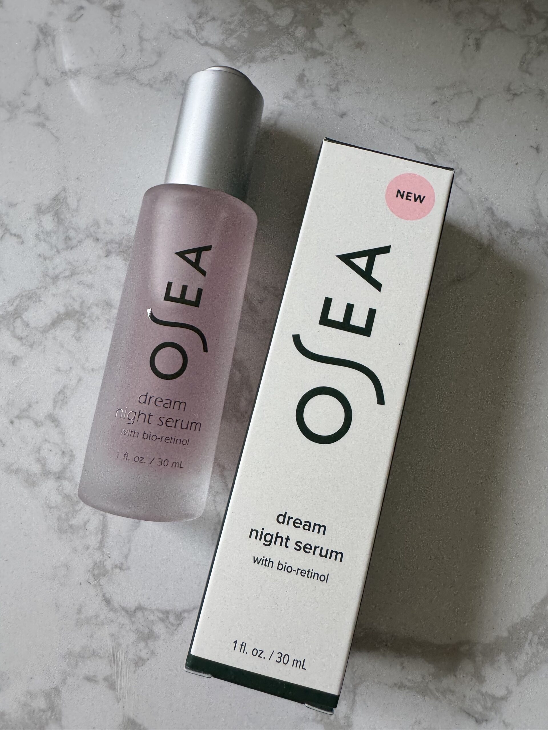 A bottle of OSEA Dream Night Serum with bio-retinol is placed next to its box on a marble surface. The box has a pink "NEW" label.