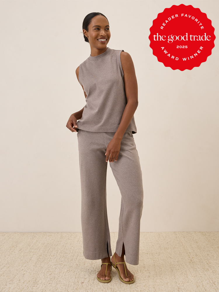 Person smiling, wearing a sleeveless top and wide-leg pants in a neutral color, standing indoors on a textured rug. "The Good Trade Award Winner 2025" badge displayed in the corner.