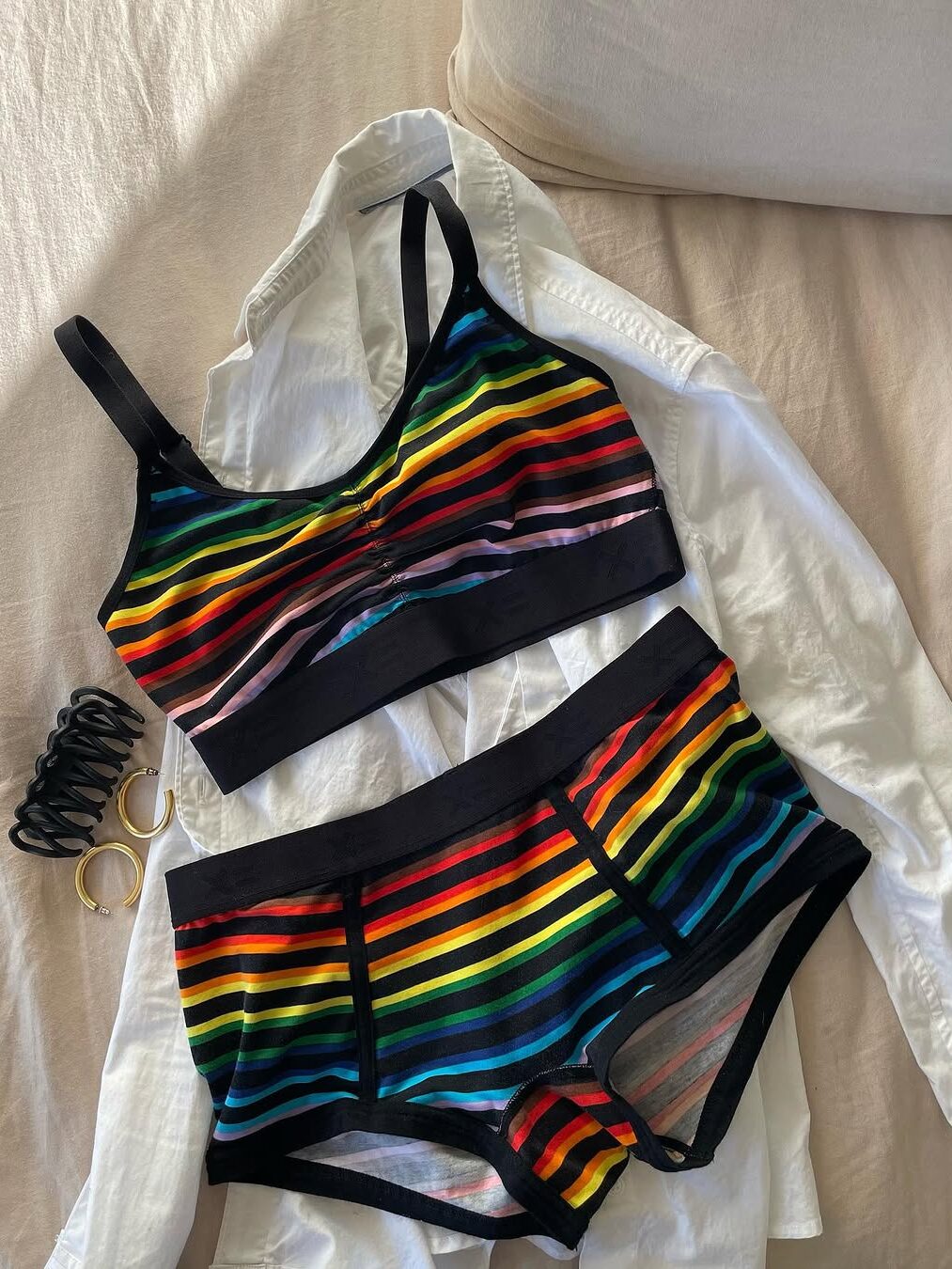 Colorful striped bra and briefs set on a white shirt, with hair ties and a gold ring nearby.