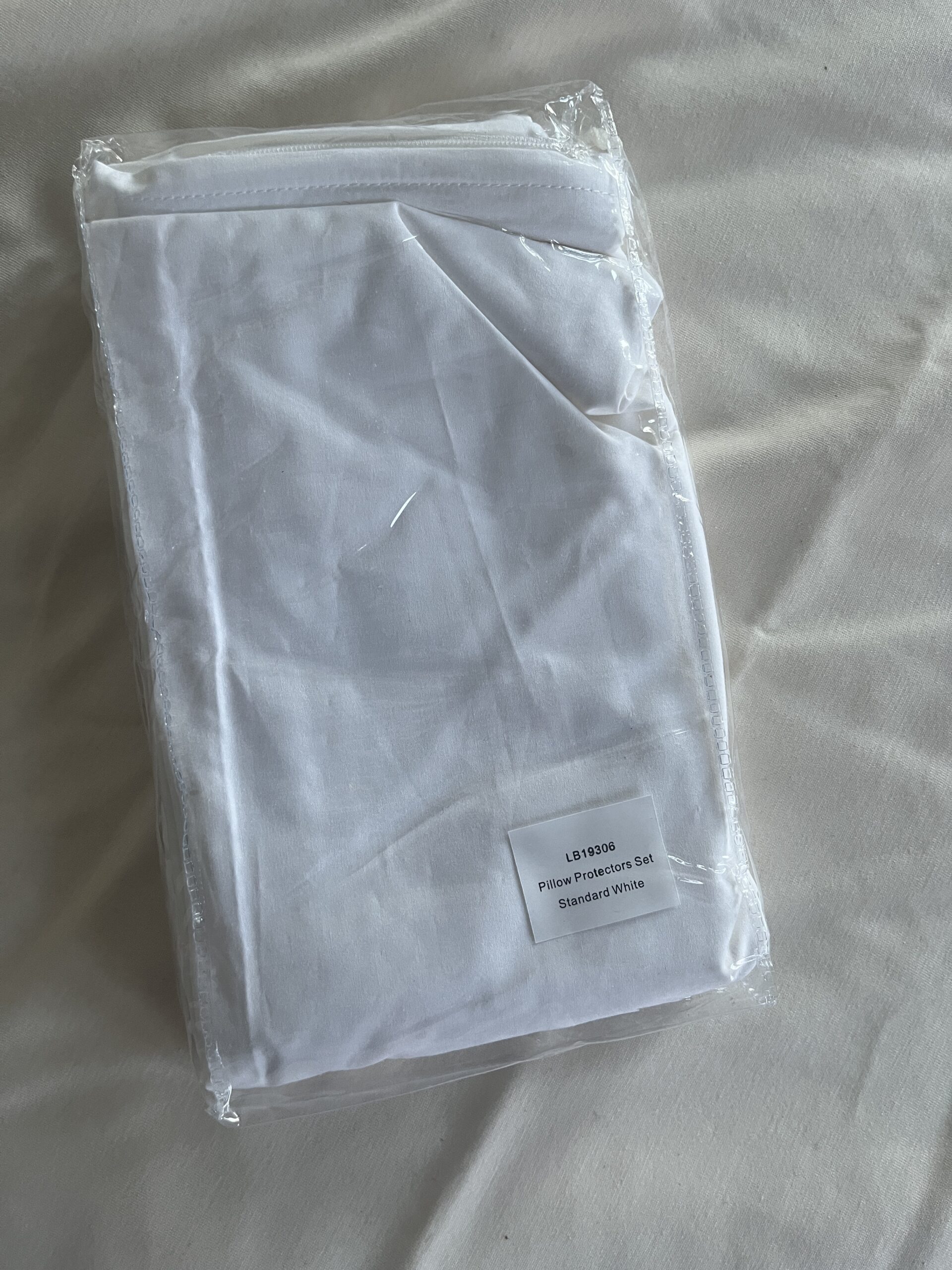 A packaged white pillow protector set is placed on a light-colored surface.
