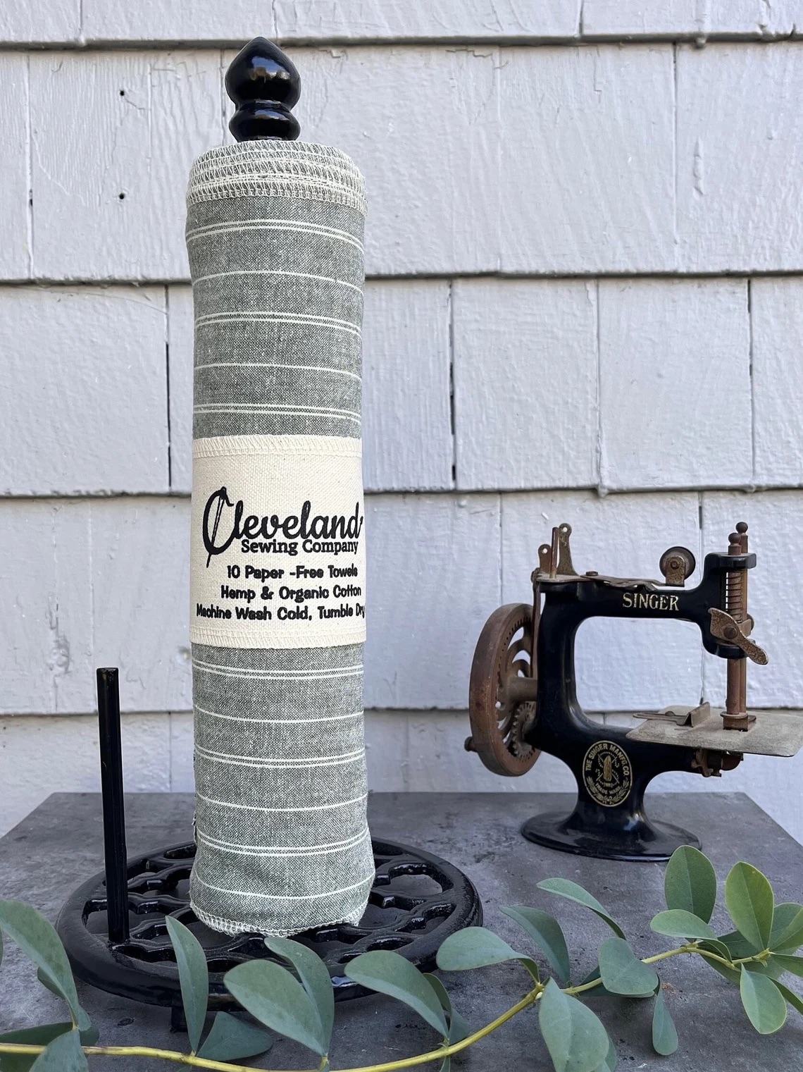 A green striped towel roll from Cleveland Sewing Company is displayed on a stand next to a vintage Singer sewing machine.