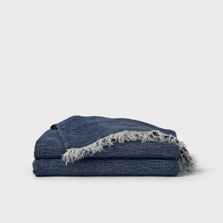 A neatly folded stack of two dark blue woven blankets with light-colored fringed edges, placed on a plain white background.