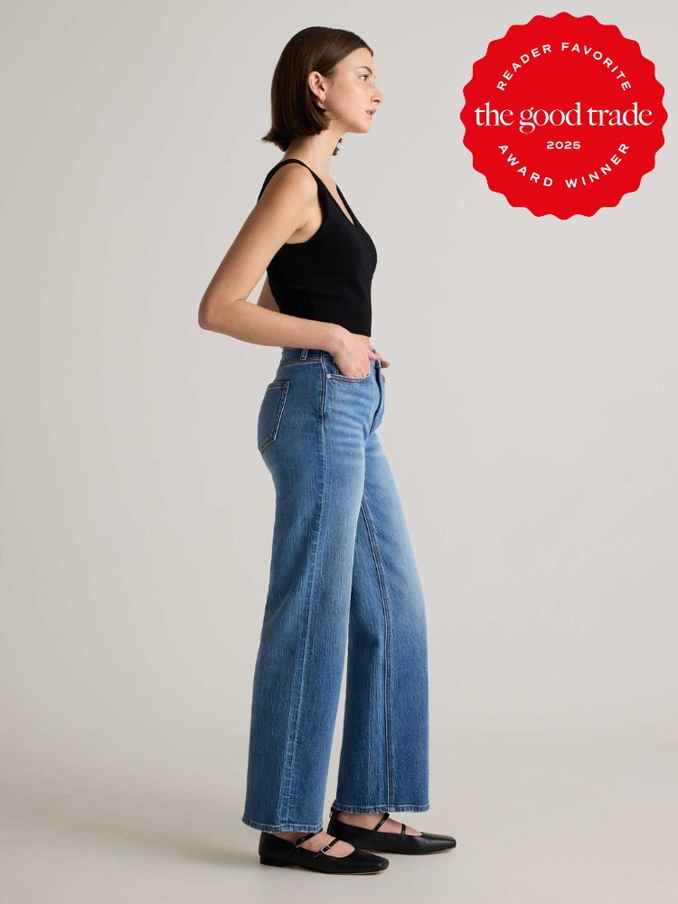 Side view of a person wearing a black tank top, blue wide-leg jeans, and black shoes. There's a red award badge in the background.