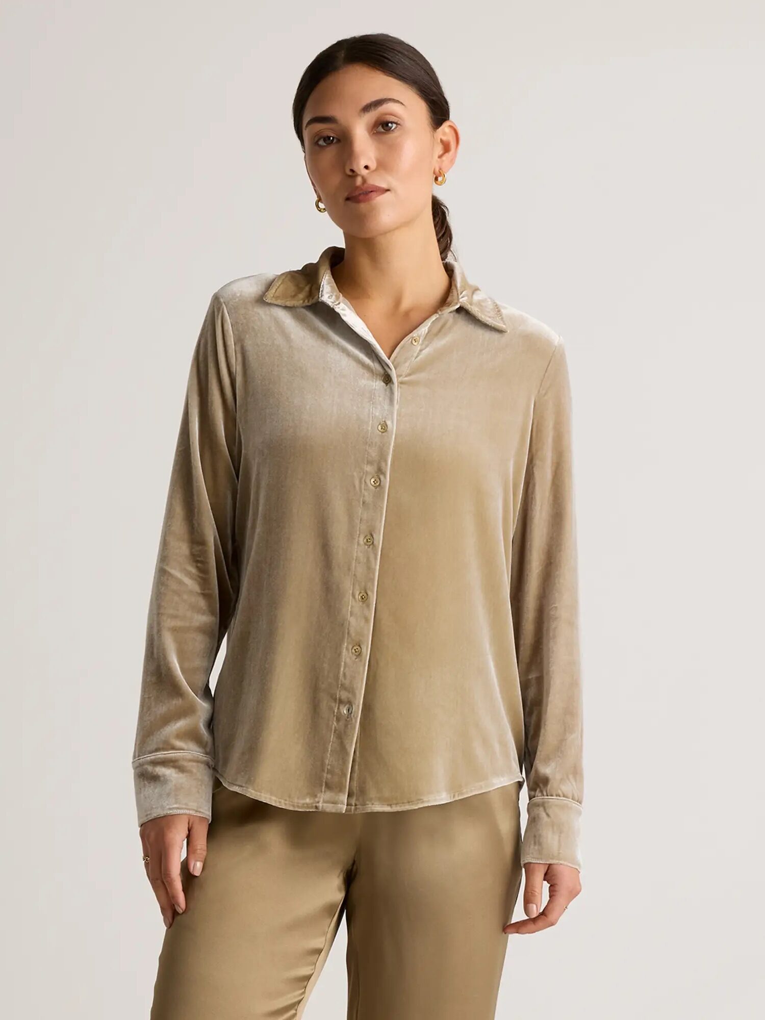 A person wearing a beige velvet long-sleeve button-up shirt and matching pants stands against a plain background.