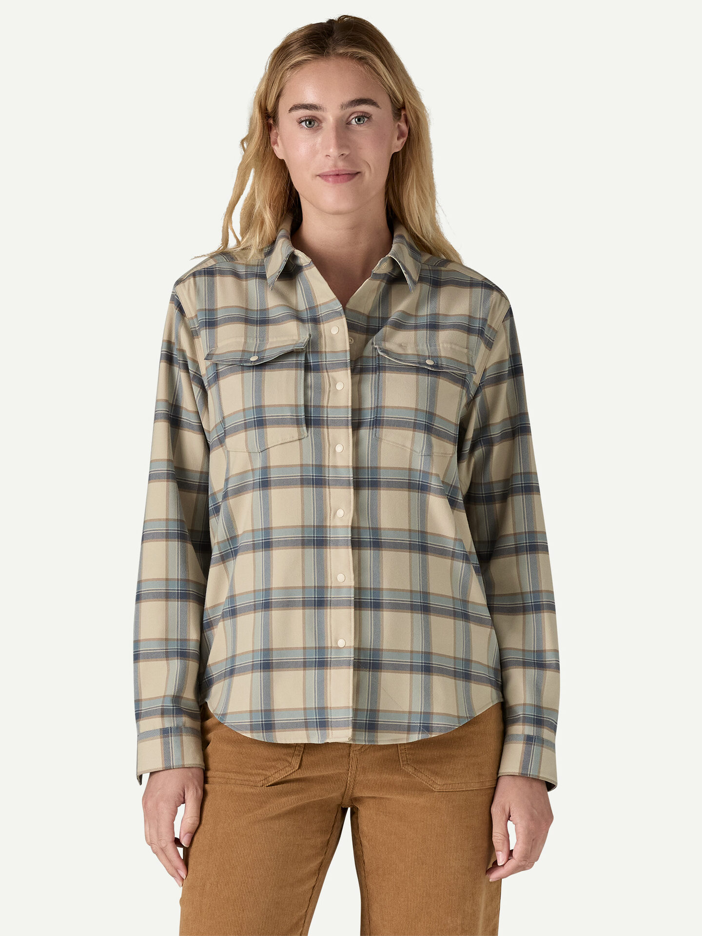 A person wearing a plaid shirt and brown pants stands against a plain background.