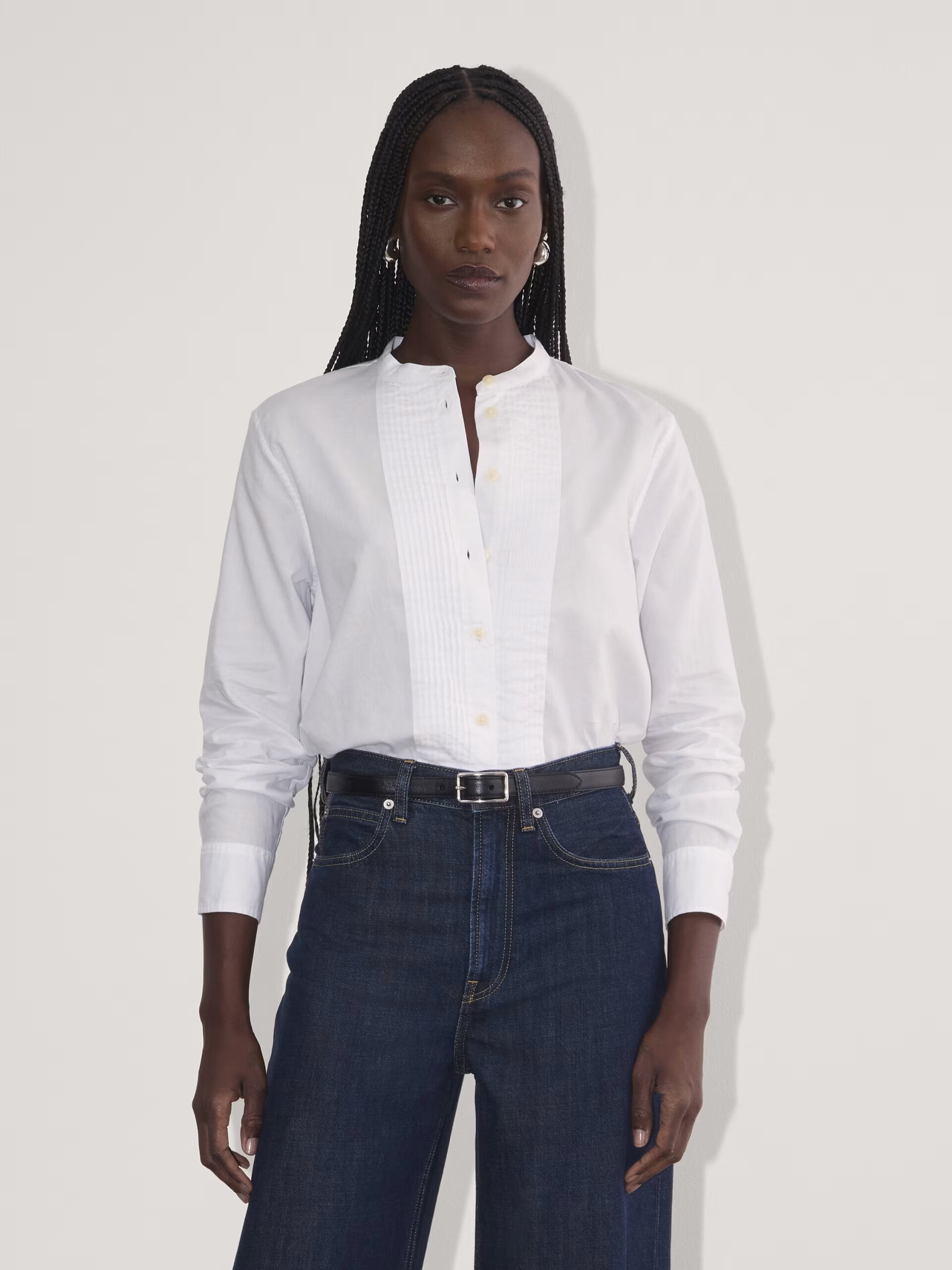 Person wearing a white button-up shirt and dark jeans, standing against a neutral background.