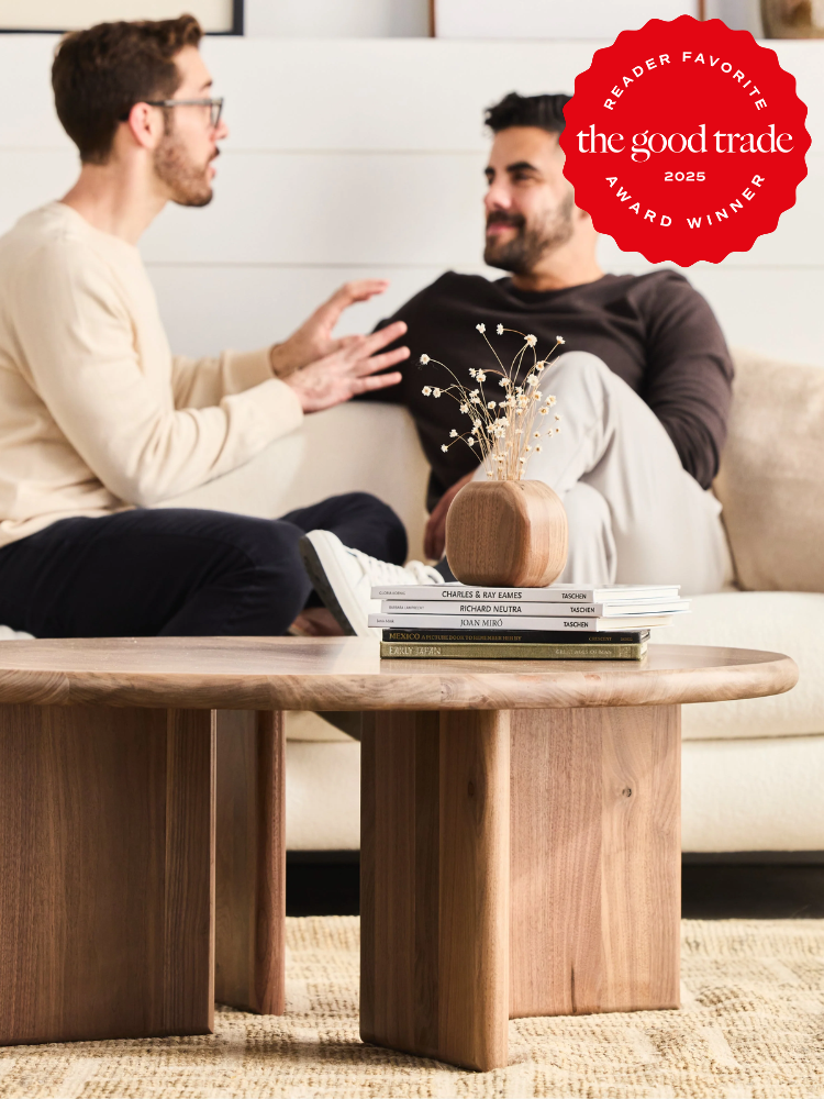 Two men sitting on a couch talking, with a wooden table and books in the foreground. A "Reader Favorite" award badge from The Good Trade is displayed in the top right corner.