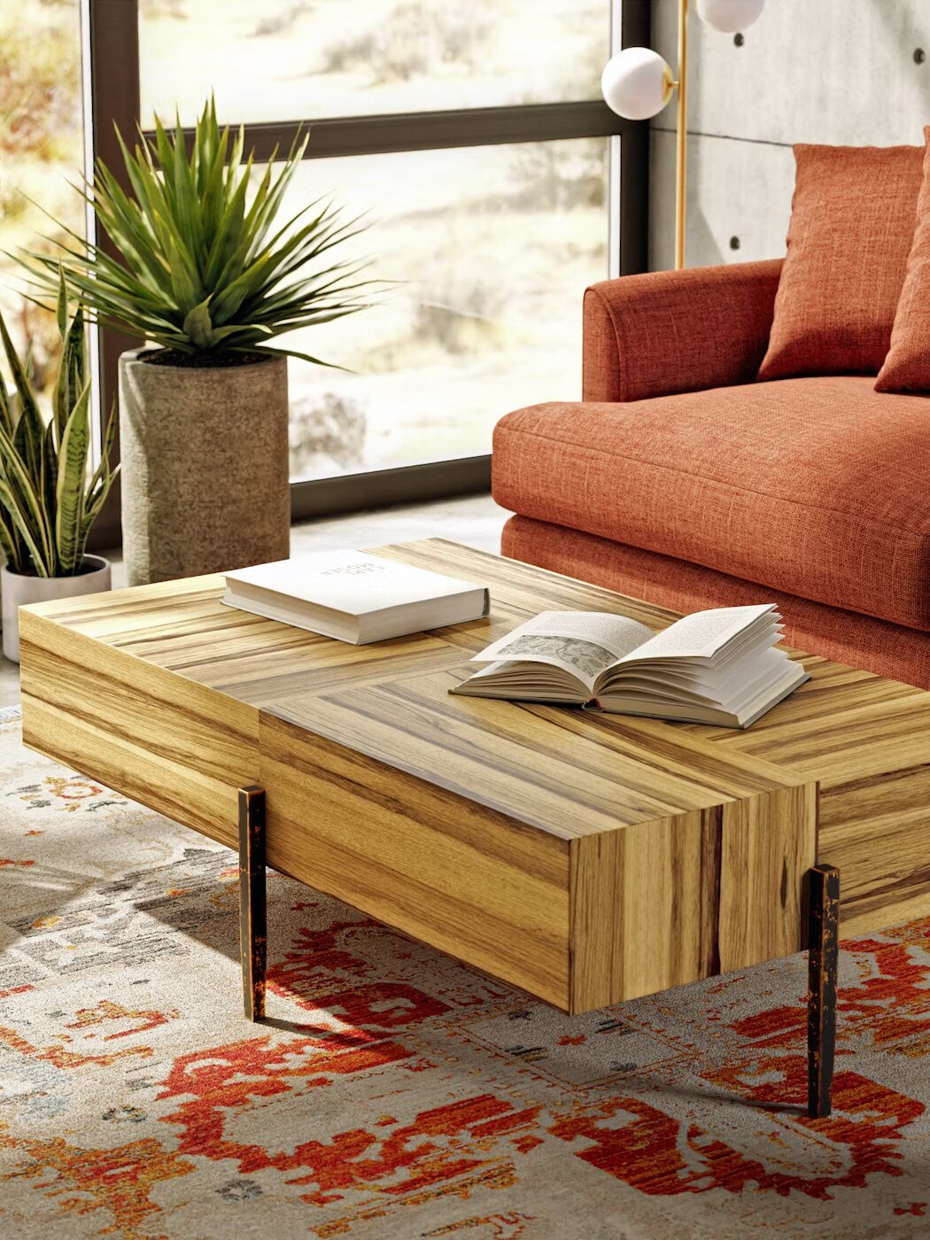 Living room with a wooden coffee table, open books, an orange sofa, green plants, and a patterned rug.