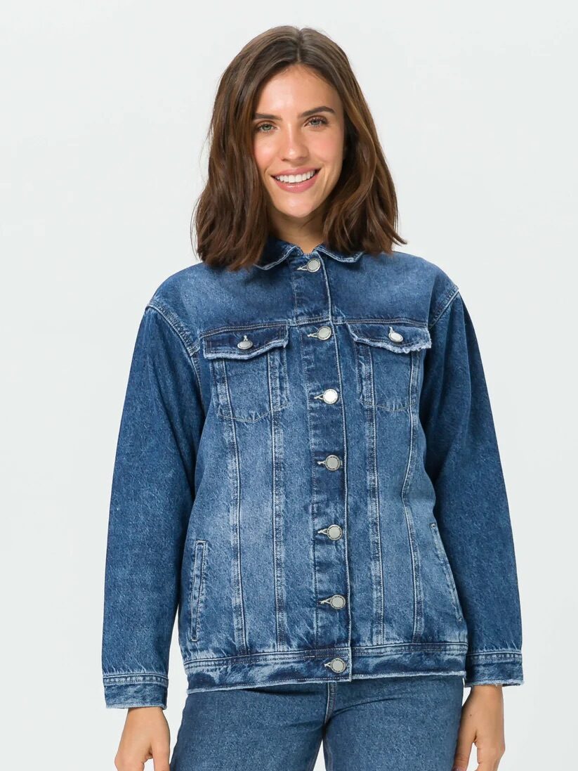 Woman wearing a denim jacket and jeans, smiling at the camera against a plain white background.