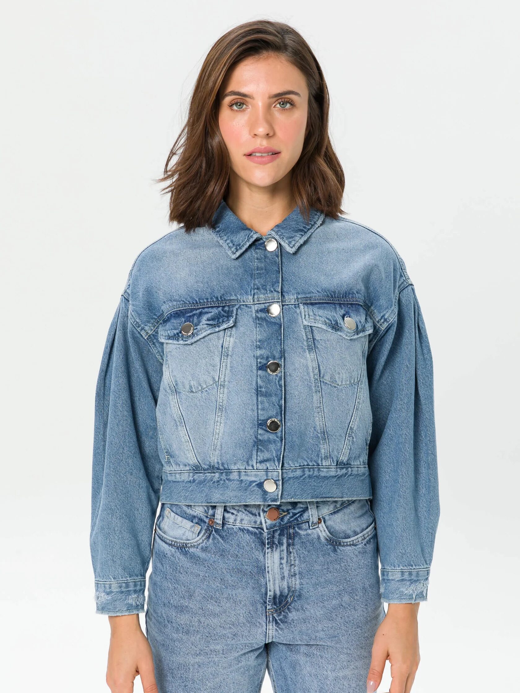 A person wearing a blue denim jacket and jeans, standing against a plain white background.