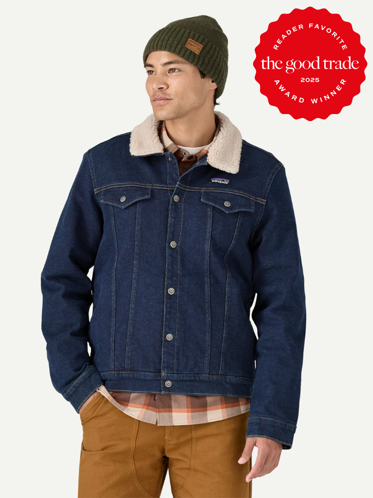 A person wearing a denim jacket with a faux shearling collar, plaid shirt, and beanie stands with hands in pockets. A red badge reads "Reader Favorite The Good Trade 2023 Award Winner.