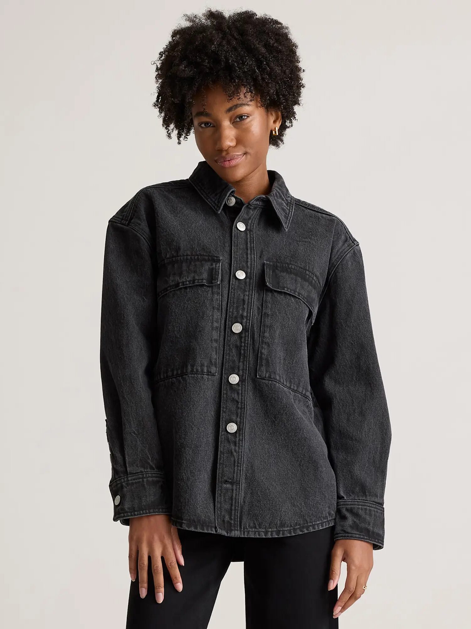 Person wearing a dark denim jacket with snap buttons, standing against a plain background.