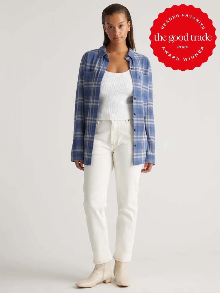 A person wearing a blue plaid shirt, white top, white pants, and beige boots stands against a plain background. A red badge in the top right reads "The Good Trade, 2023 Reader Favorite Award Winner.