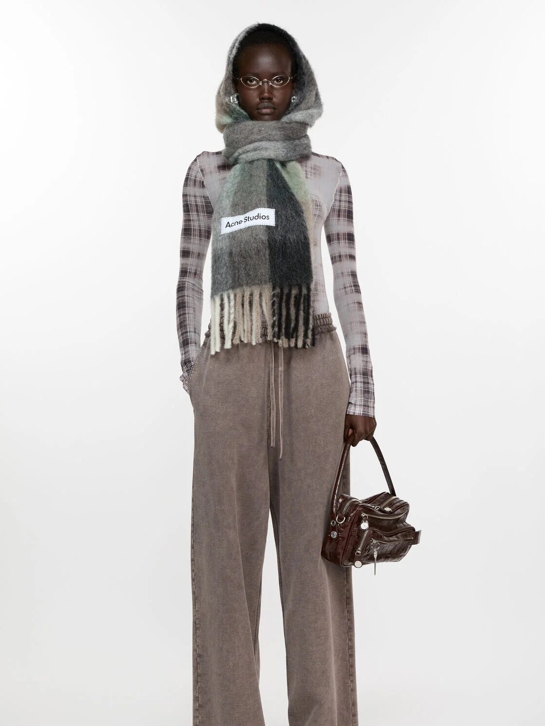 Person wearing a plaid top, large scarf, and wide-leg pants, holding a handbag.