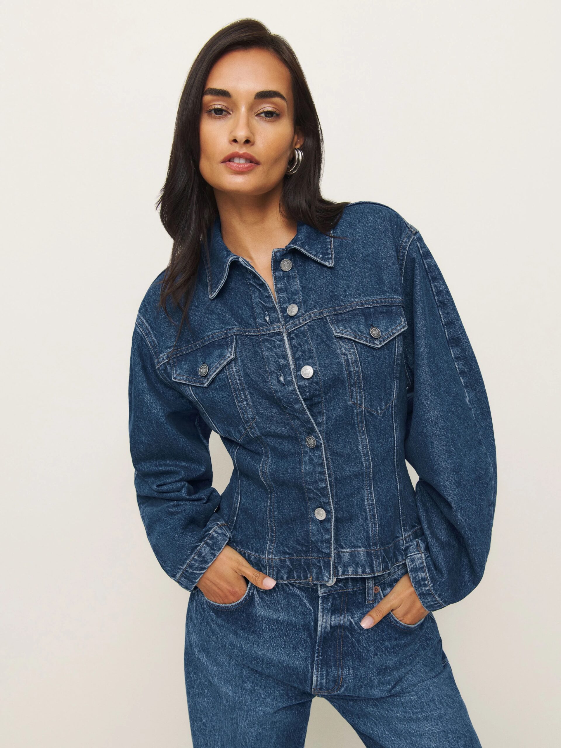Person posing in a denim jacket and jeans against a plain background.