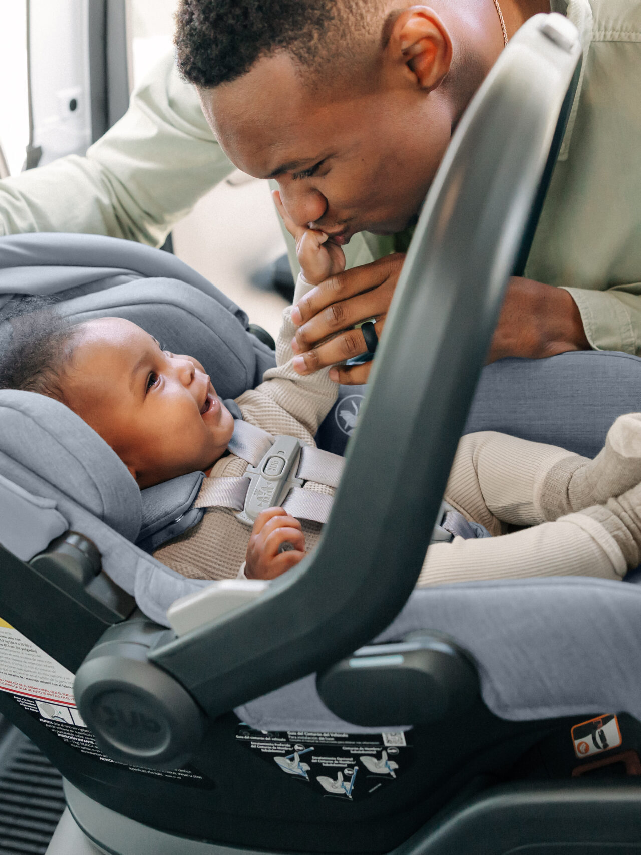 A man gently cares for a baby secured in a gray car seat inside a vehicle.