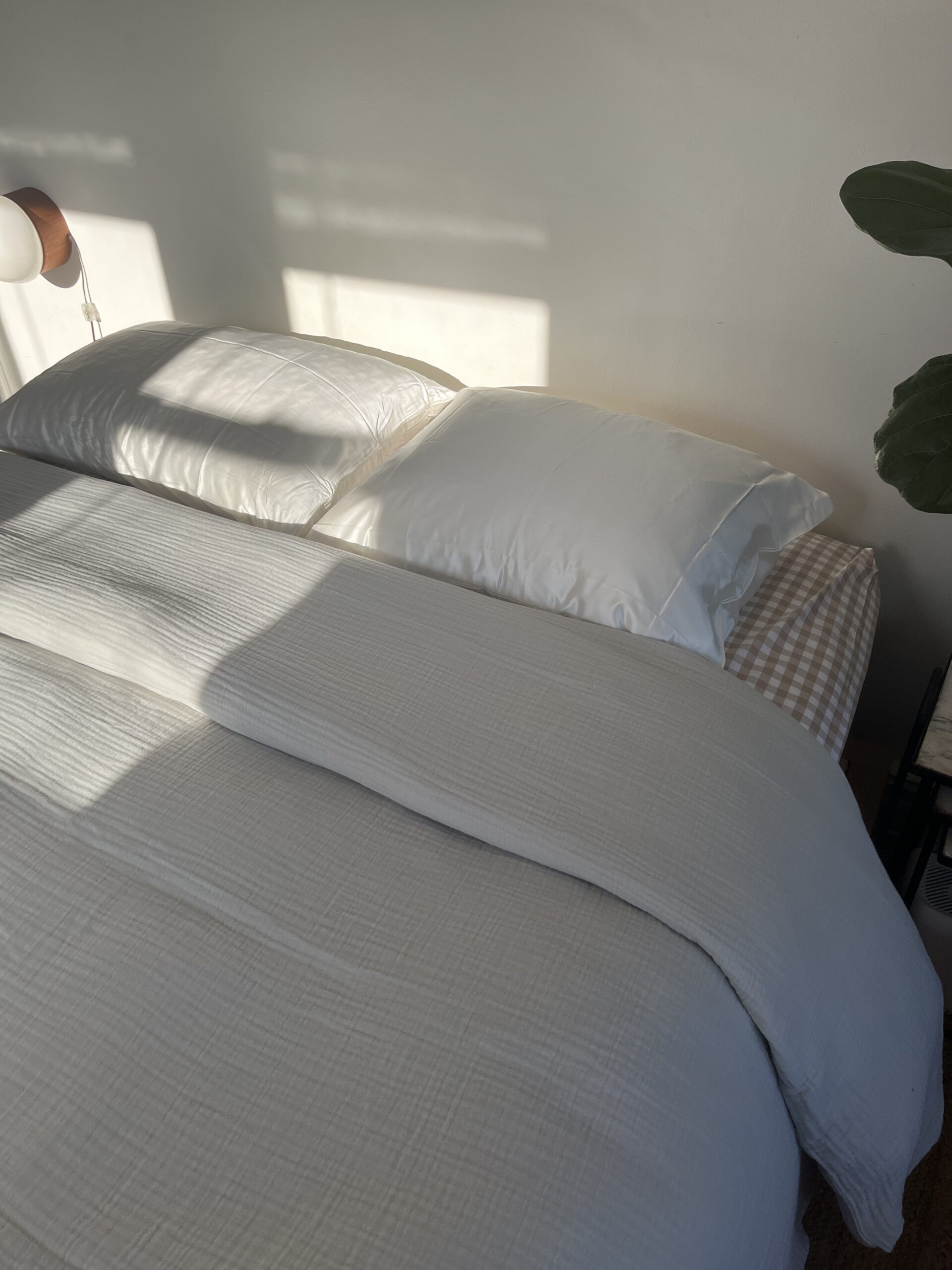 A neatly made bed with white bedding and two pillows, illuminated by natural sunlight coming through a window, casting shadows on the bed.