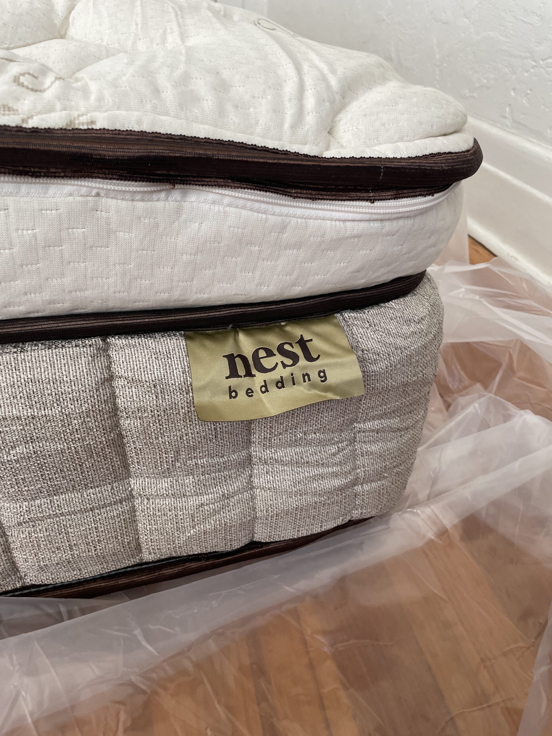 A Nest Bedding mattress is shown on a hardwood floor, partially wrapped in transparent plastic.