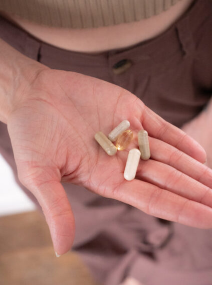 Hand holding a small assortment of capsules and pills, including a clear gel capsule, against a blurred background.