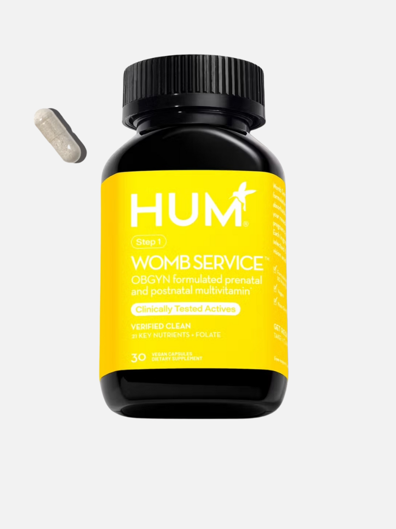 A bottle of HUM "Womb Service" prenatal and postnatal multivitamin with a capsule beside it. The label highlights clinically tested actives and verified clean nutrients.